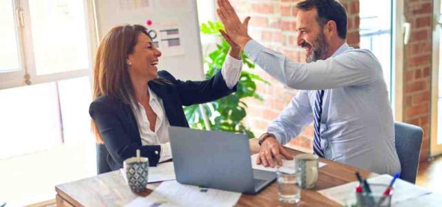 Two people at work high fiving at a desk